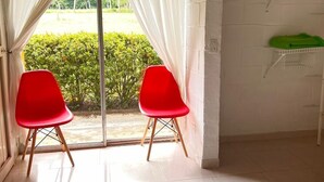 Ein Zimmer mit einer Schiebeglastür, zwei roten Stühlen, einem weiß gefliesten Boden und einer weißen Ziegelwand.