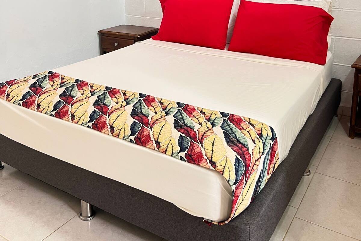 A bed with a colorful leaf-patterned bedspread, a wooden headboard, and red pillows.