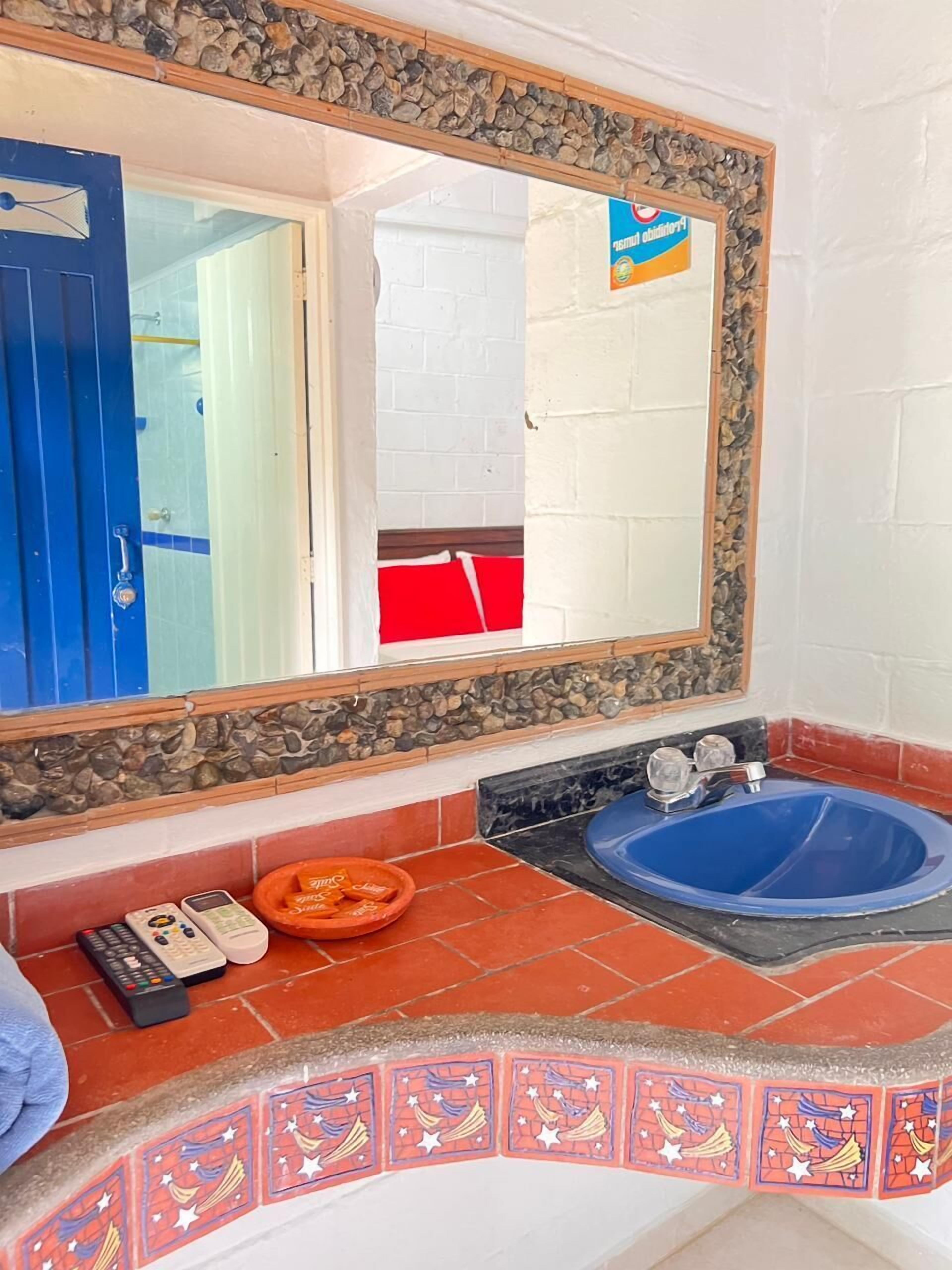 Un baño con un lavabo azul, un espejo con marco de piedra, una toalla roja y una puerta azul.