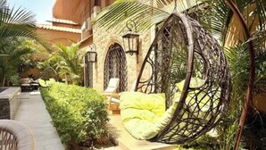 A patio area with a hanging chair, a bench, and a pathway leading to a building with a stone facade and arched windows. - 2BRs with garden- Three Sisters Villa 3 (New Cairo City)
