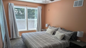 Un dormitorio con una cama, dos mesitas de noche, una ventana con cortinas y un ventilador de techo.