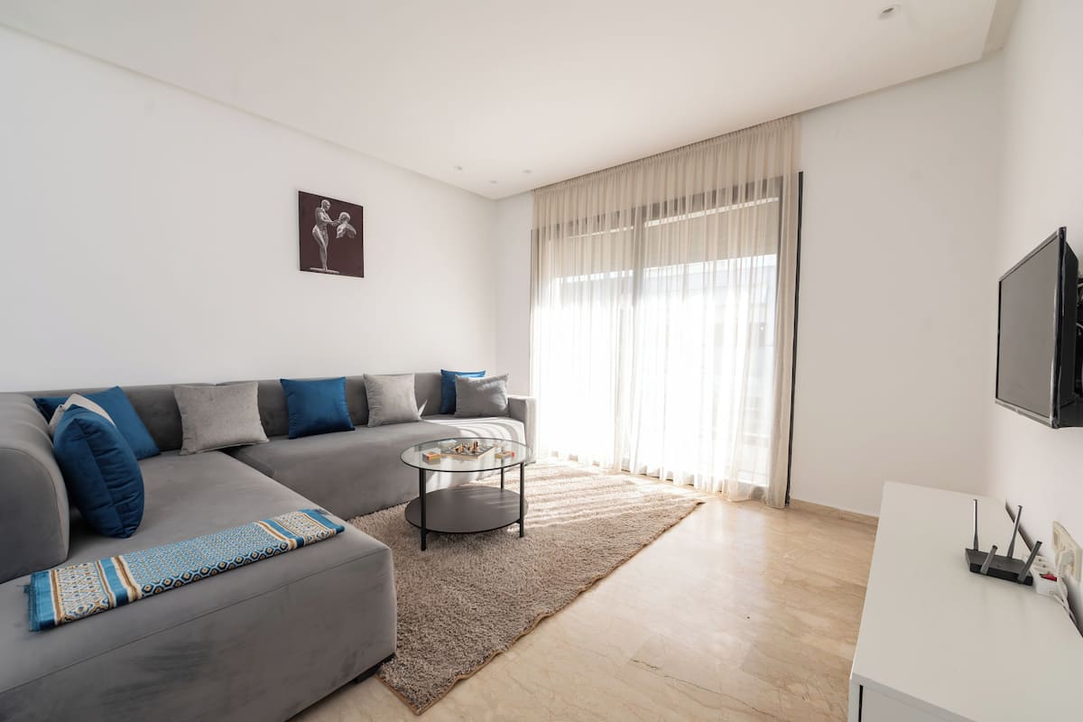 A modern living room with a grey sectional sofa, a glass coffee table, and a white TV stand.