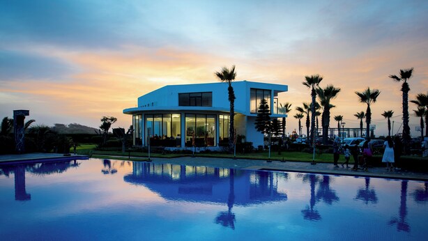 A modern hotel with a pool, palm trees, and a sunset view. - Garden Bay Signature AppartHotel (Sidi Rahal)