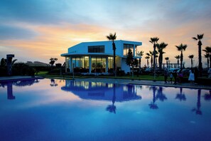 Un hotel moderno con piscina, palmeras y vistas al atardecer.