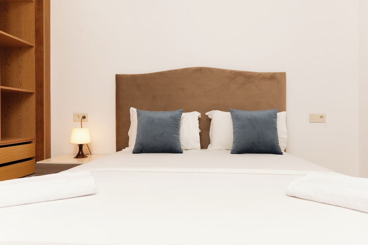 Una cama bien hecha con un cabecero marrón, dos almohadas y una lámpara de noche.