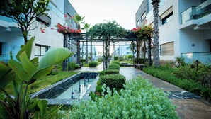 A courtyard with a central water feature, surrounded by lush greenery and modern buildings. - Garden Bay Signature AppartHotel (Sidi Rahal)
