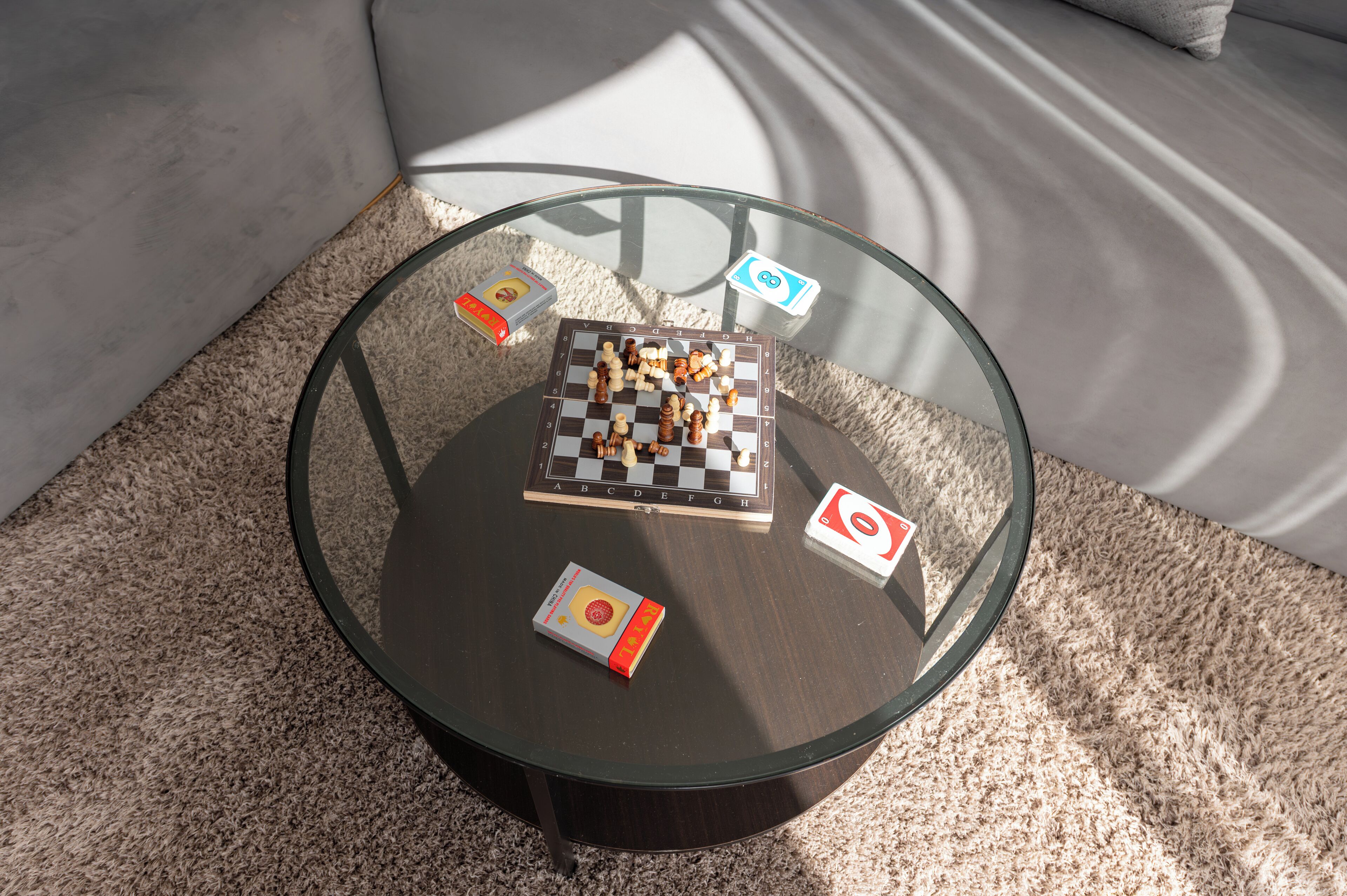 Een ronde glazen tafel met een schaakbord, twee boeken en twee speelstukken.