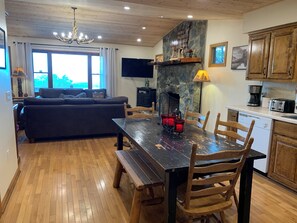 A cozy living room with a dark sofa and wooden dining table, a stone fireplace, and wooden cabinets. - Amazing view,sleeps 7 hot tub,Wi-Fi, game room,fire pit total privacy on 4 acres (Murphy)