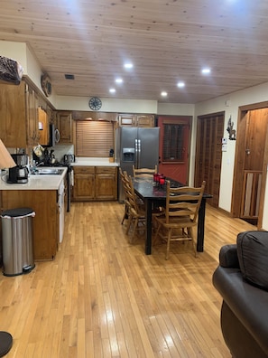 A kitchen with wooden cabinets, a stainless steel refrigerator, a dining table with chairs, and a trash can. - Amazing view,sleeps 7 hot tub,Wi-Fi, game room,fire pit total privacy on 4 acres (Murphy)