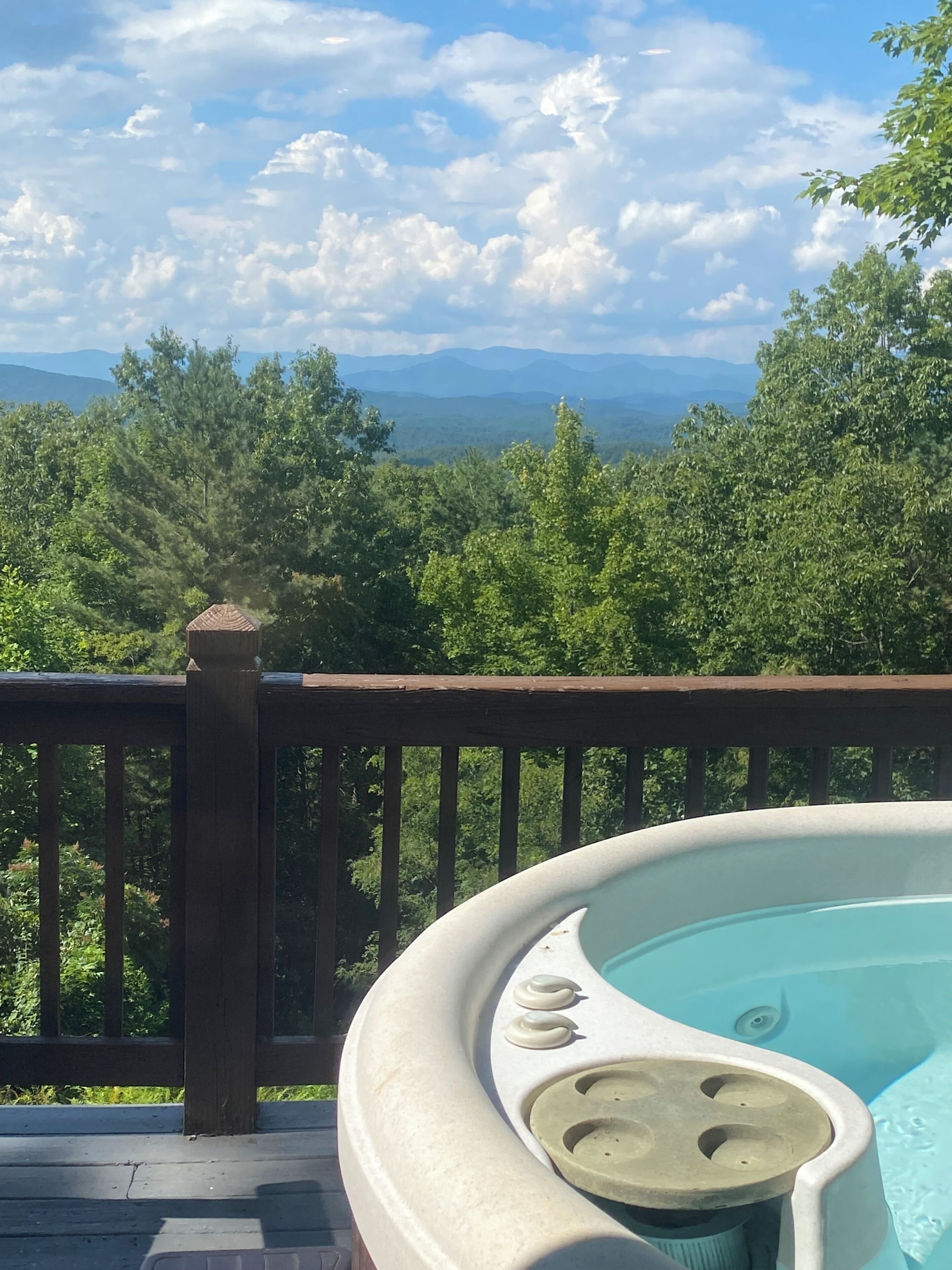 A hot tub on a deck with a view of mountains and trees.