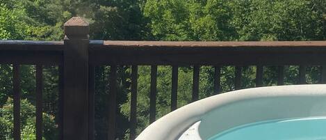 A hot tub on a deck with a view of mountains and trees.