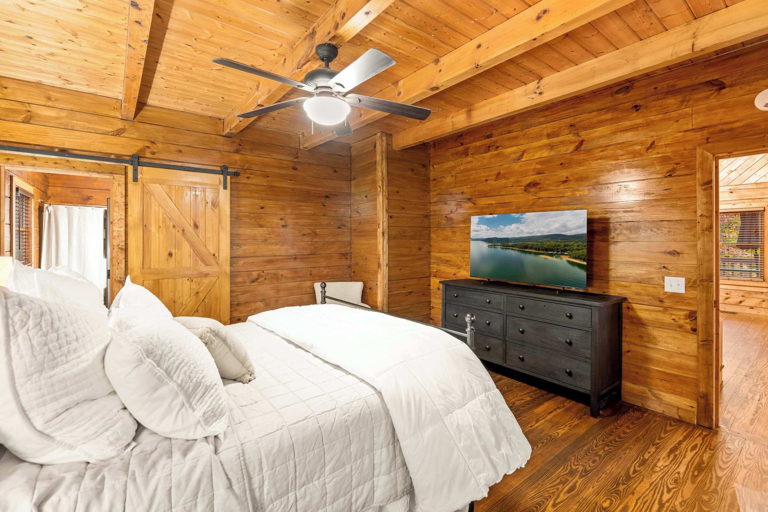 Camera da letto in una baita di legno, con un letto, una cassettiera, una ventola a soffitto e un televisore appeso al muro.