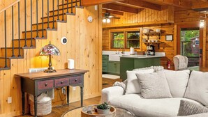 A spacious living area with a wooden staircase, a sofa, a coffee table, and a kitchen in the background. - Luxury Cabin in beautiful Wears Valley (Sevierville)