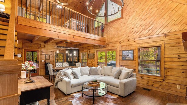 A spacious living room with a large sectional sofa, a glass coffee table, and a wooden ceiling. - Luxury Cabin in beautiful Wears Valley (Sevierville)