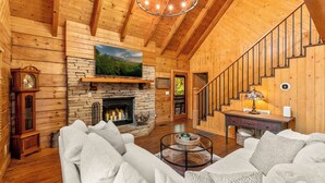 A log cabin interior with a stone fireplace, wooden staircase, and a cozy seating area. - Luxury Cabin in beautiful Wears Valley (Sevierville)