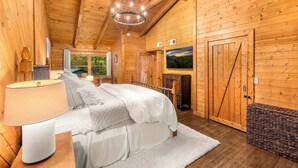 A wooden cabin bedroom with a bed, a nightstand, a lamp, a dresser, a window, and a door. - Luxury Cabin in beautiful Wears Valley (Sevierville)