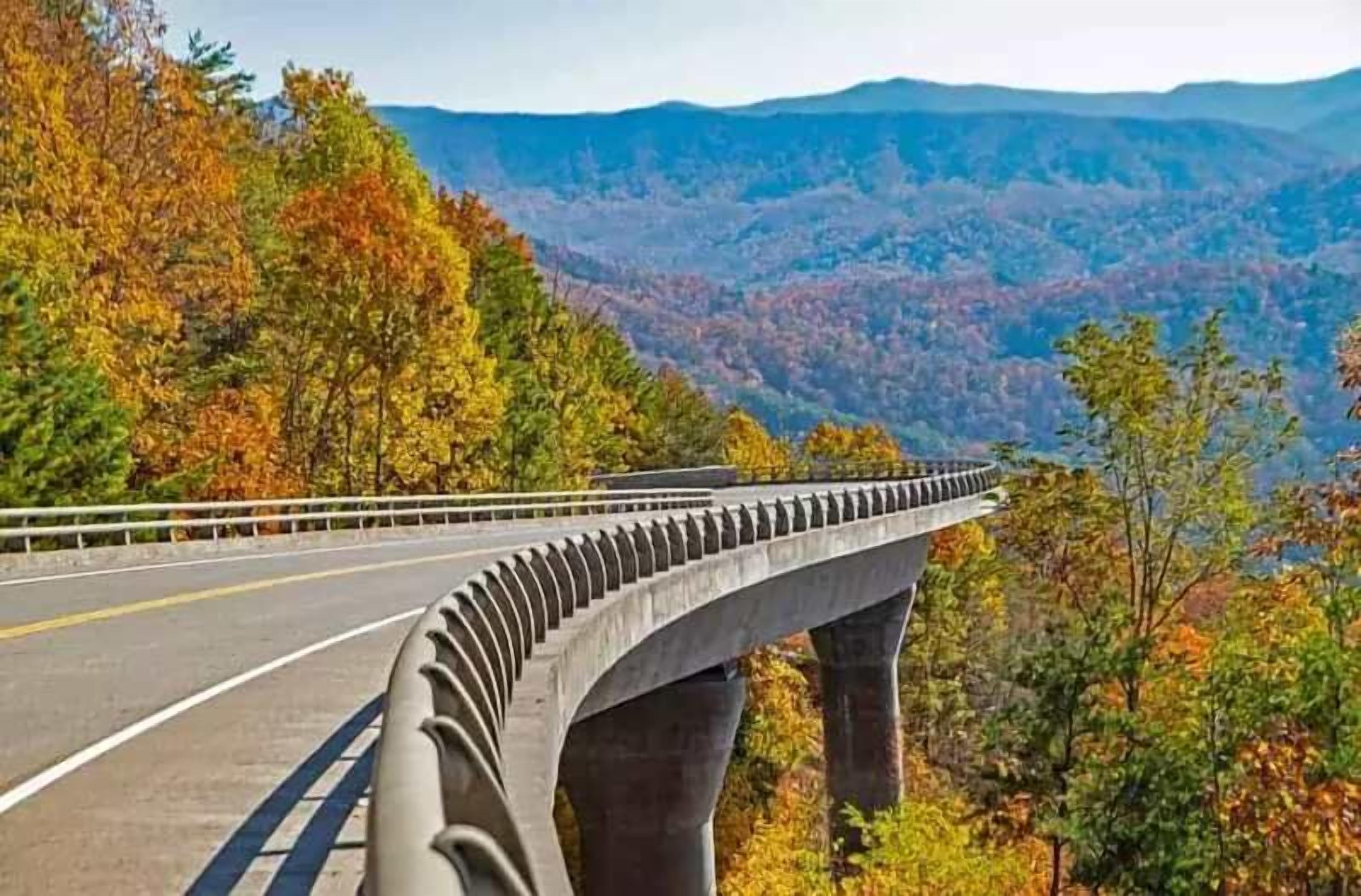 A bridge with a guardrail, surrounded by autumn foliage and a mountainous landscape.
