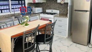 A kitchen with white cabinets, a stainless steel refrigerator, a microwave, and a gas stove. There is a dining table with chairs and a potted plant on it. - Small apartment-style villa near the beach (Puerto Plata)