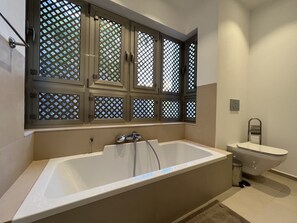A bathroom with a bathtub, toilet, and a window with a lattice design.