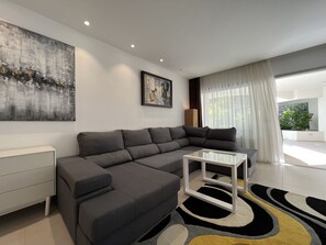 A modern living room with a sectional sofa, a glass coffee table, and a large abstract painting on the wall.