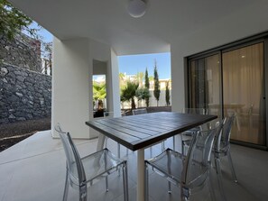 A modern outdoor patio with a table and chairs, a stone wall, and a view of palm trees.