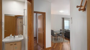 Un interior moderno con suelo de madera, una zona de comedor con mesa y sillas, y un baño con lavabo y espejo.
