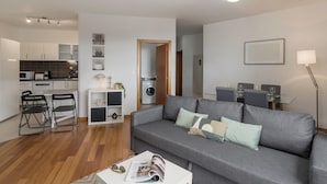 Una sala de estar moderna con un sofá gris, una mesa de centro y un comedor con una mesa y sillas. Hay una cocina con armarios y un microondas.