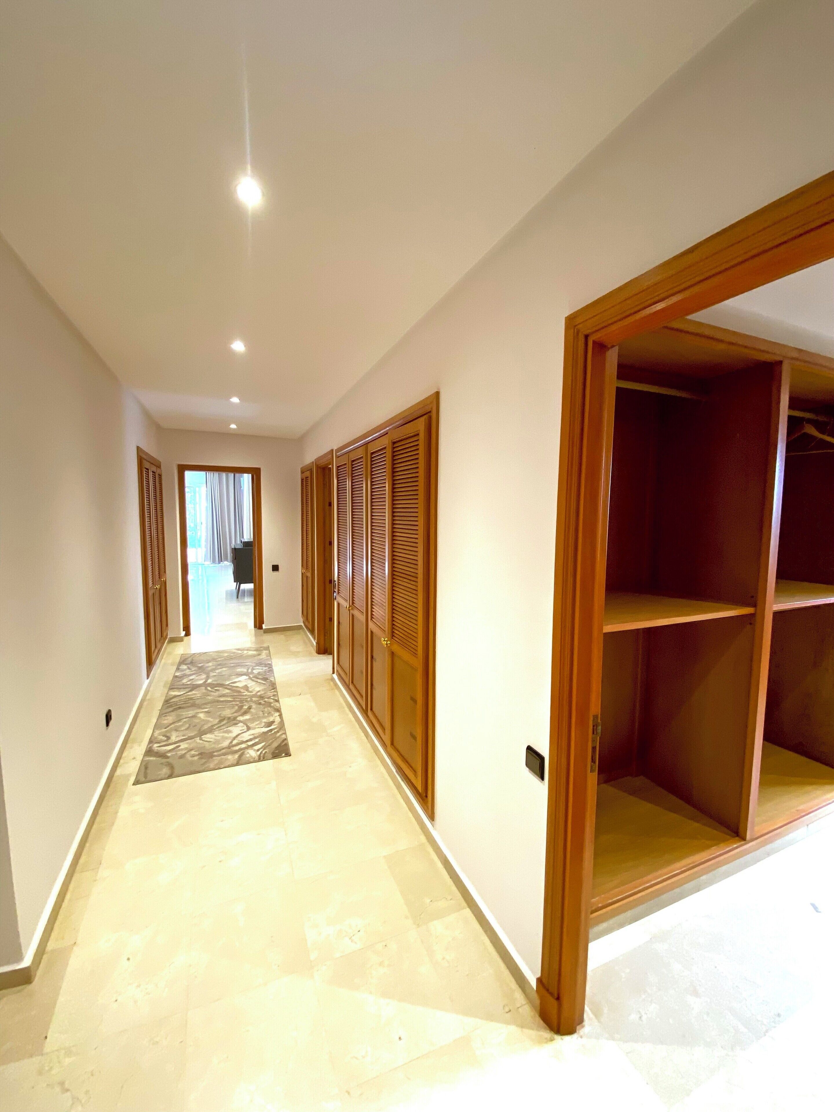 A hallway with a wooden closet and a view into another room.
