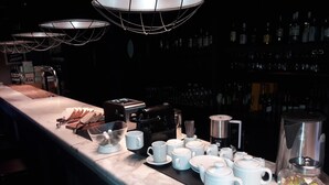 Una zona de bar con una máquina de café, teteras y una variedad de tazas en la barra.