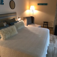 Una cama bien hecha con un almohadón esponjoso y una lámpara a un lado.