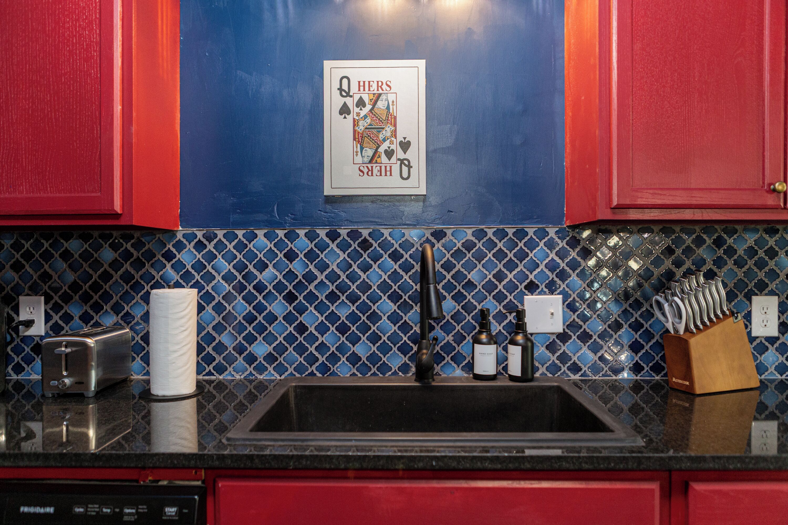 A kitchen with red cabinets, a sink, a toaster, and a paper towel dispenser.