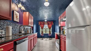A kitchen with red cabinets, a stainless steel refrigerator, and a window with red curtains. - We're All Mad Here! - A Wonderland Escape in Tulsa (Tulsa)