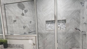Un baño moderno con ducha envuelta en vidrio, encimeras de granito y una salpicadera de mármol.