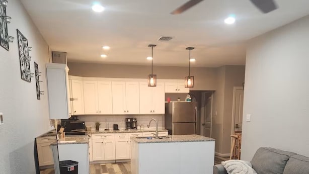 Una sala de estar moderna con un sofá gris, una mesa de centro de madera y un mueble para el televisor. Se ve la zona de la cocina con armarios blancos y una isla central.
