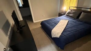 Un dormitorio con cama, escritorio y silla. Hay una puerta que da a otra habitación.