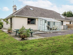 A single-story house with a conservatory, a garden with a green lawn, and a picnic table. - LILLY'S BUNGALOW, pet friendly in Clonakilty, County Cork (Timoleague)