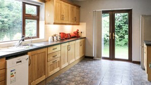 A kitchen with wooden cabinets, a dishwasher, a sink, and a window overlooking greenery. - LILLY'S BUNGALOW, pet friendly in Clonakilty, County Cork (Timoleague)