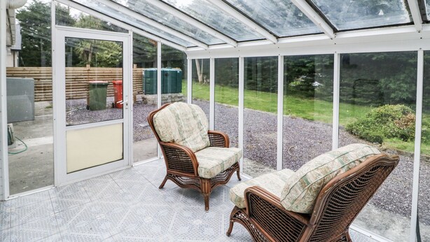 A conservatory with wicker furniture and a view of the garden. - LILLY'S BUNGALOW, pet friendly in Clonakilty, County Cork (Timoleague)