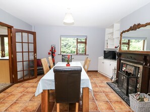 A dining area with a table, chairs, a vase with flowers, a fireplace, and a television. - LILLY'S BUNGALOW, pet friendly in Clonakilty, County Cork (Timoleague)