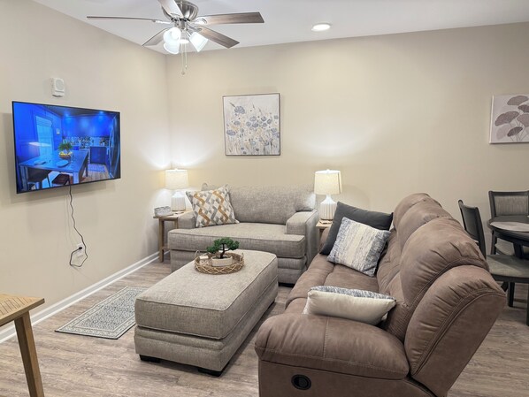 A modern living room with a flat-screen TV, two sofas, a coffee table, and a ceiling fan.