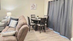 A living room with a brown sofa, a dining table with chairs, a lamp, and a grey curtain.