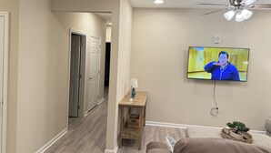 A living room with a television mounted on the wall, a ceiling fan, and a small table with a lamp.