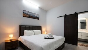 Un dormitorio moderno con una cama grande, lámparas de noche, un cuadro en la pared y una puerta corredera hacia un baño.