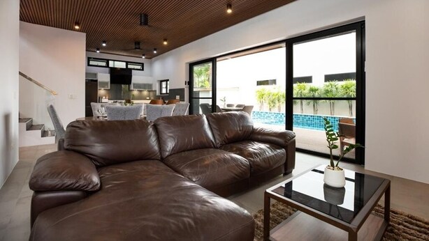Una sala de estar moderna con un sofá de cuero, una mesa de centro de vidrio y vistas a una piscina.