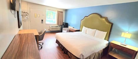 A hotel room with a bed, desk, chair, bedside table, and a television.