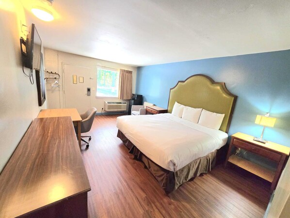 A hotel room with a bed, desk, chair, bedside table, and a television. - Brentwood Inn Richmond South (Richmond)