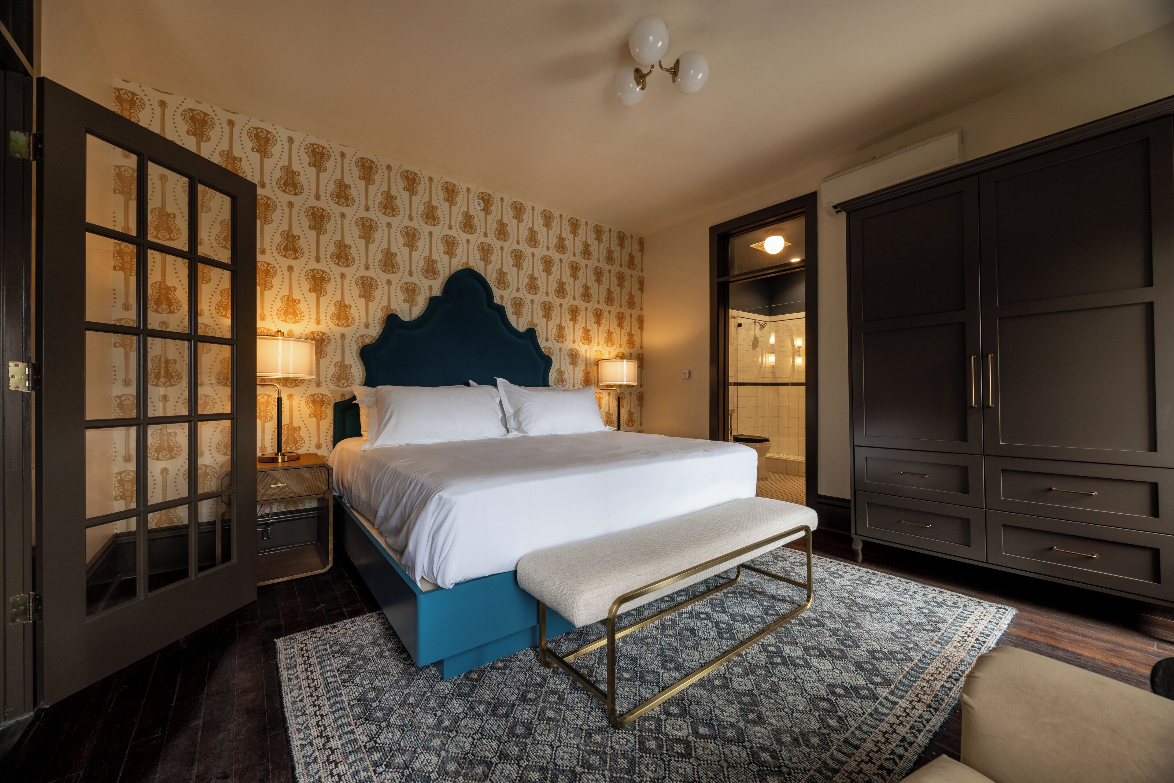 A bedroom with a large bed, a bench, a wardrobe, and a nightstand with lamps.