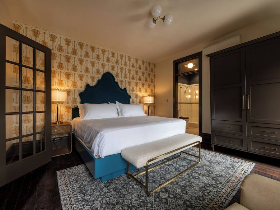 A bedroom with a large bed, a bench, a wardrobe, and a nightstand with lamps.