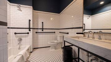 A modern bathroom with white subway tiles, a black and white patterned floor, a large mirror, a bathtub, a toilet, and a sink with a marble countertop.
