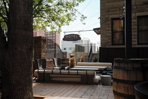 A hotel patio with outdoor seating, a sign indicating the hotel name, and a view of the cityscape in the background.
